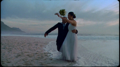 a bride and groom on the beach holding flowers