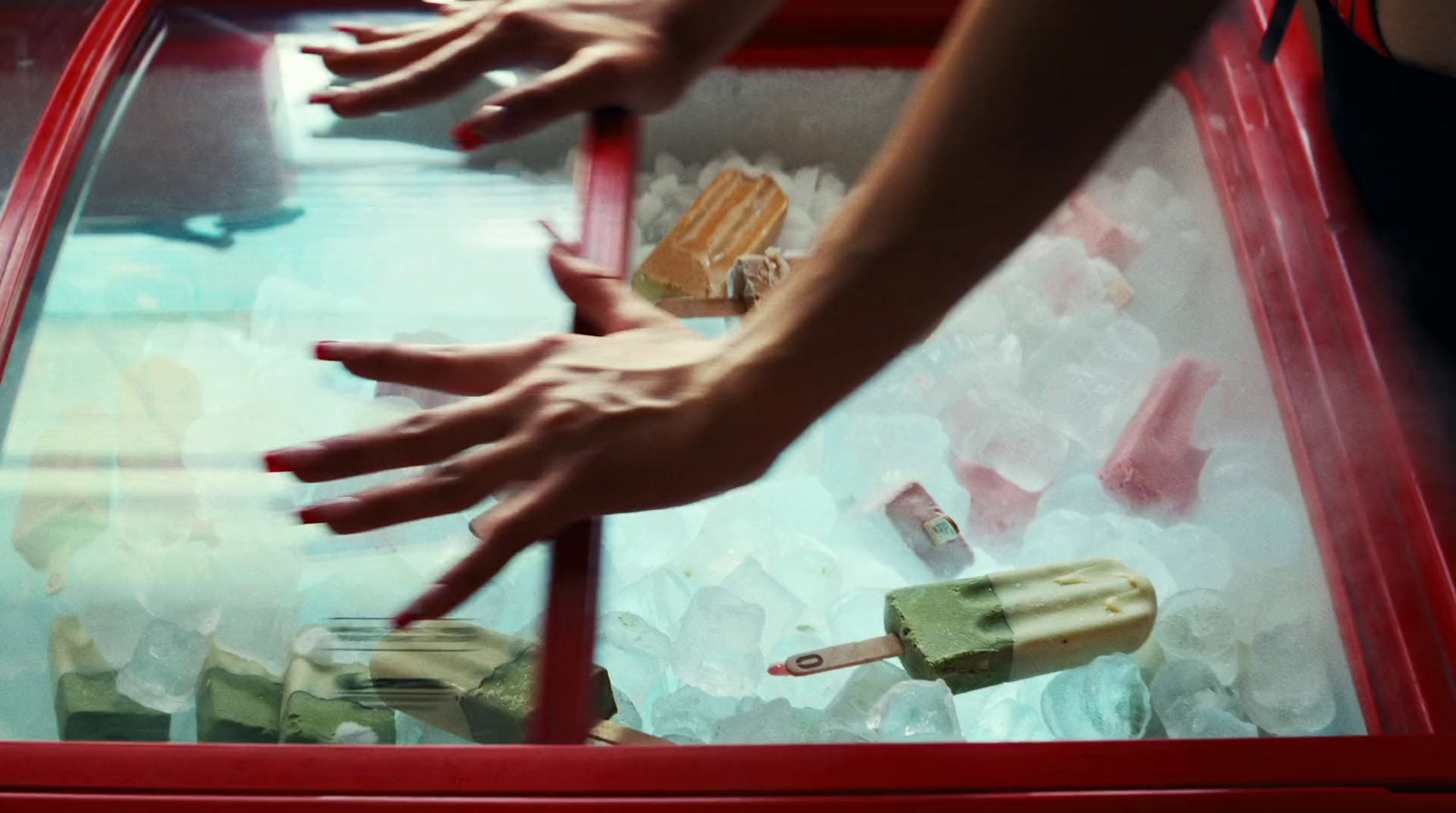 two hands reaching for a piece of cake in a display case