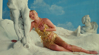 a woman in a gold dress sitting in the sand