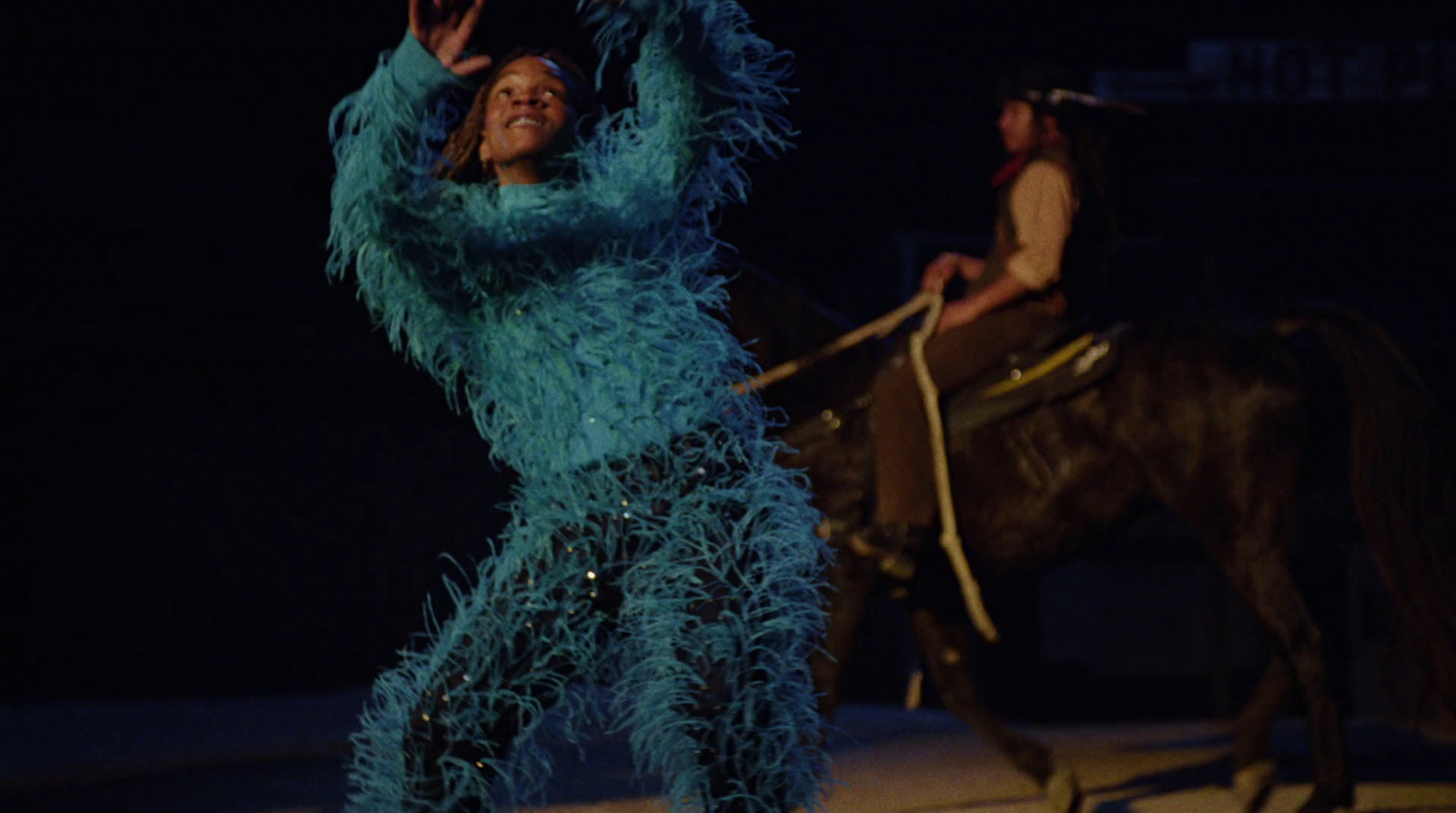 a woman in a blue feathered outfit riding a horse