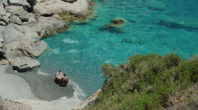 a couple of people are sitting on some rocks by the water