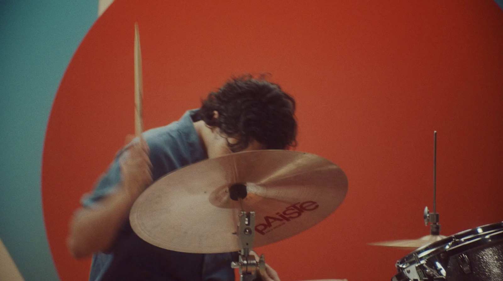 a man playing drums in front of a red wall