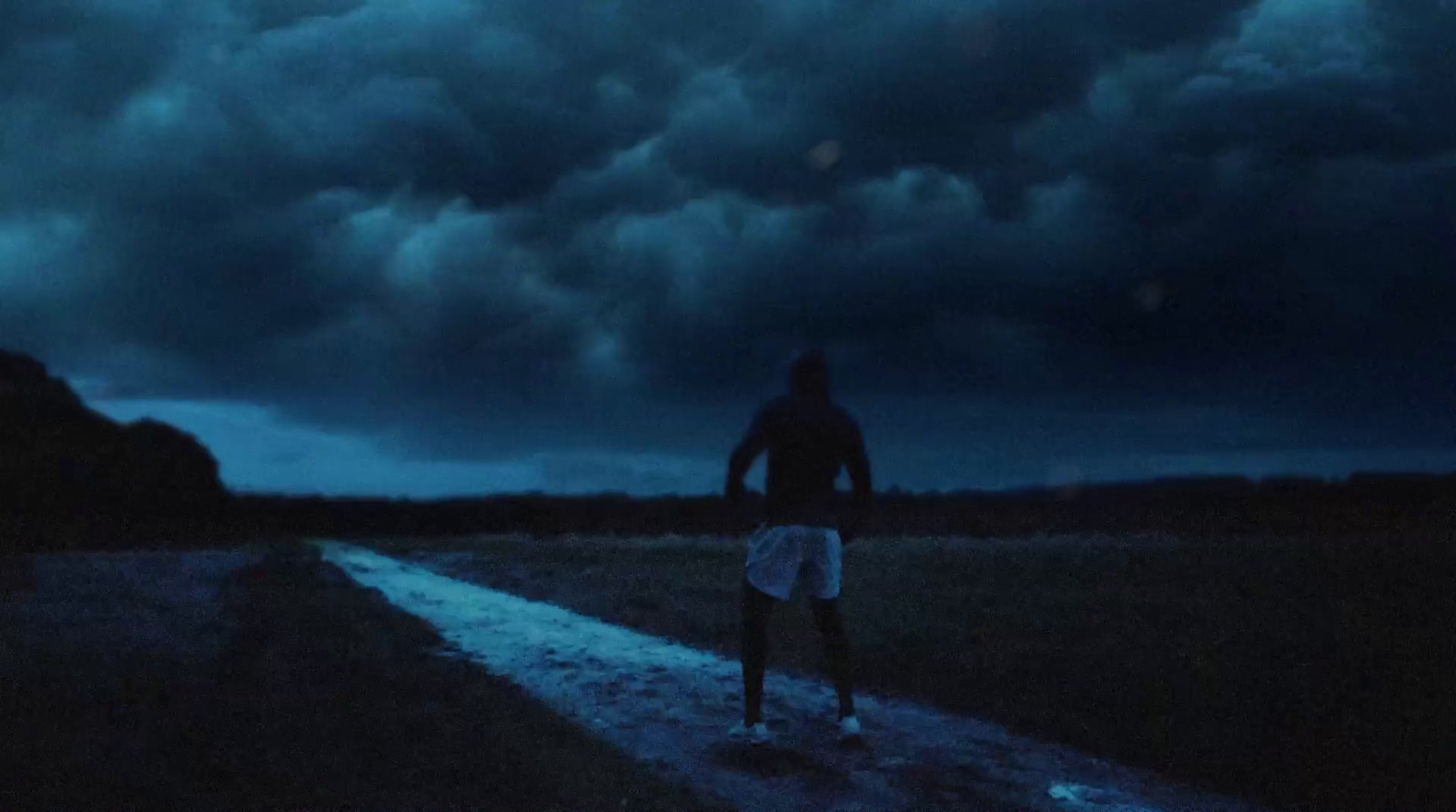 a man walking down a dirt road under a cloudy sky