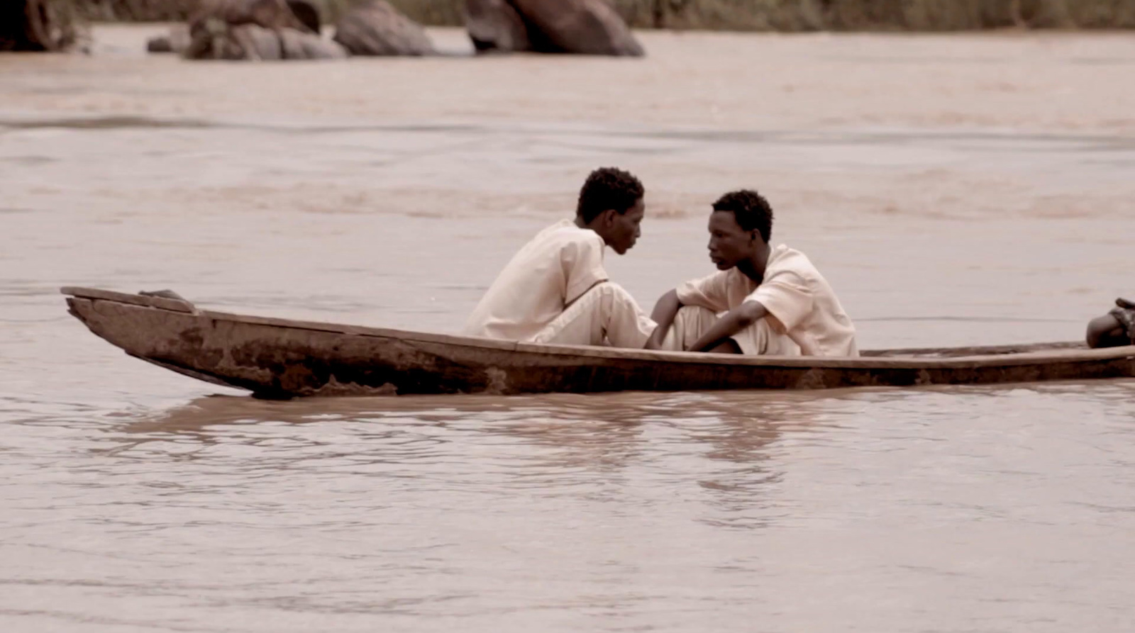 two men sitting in a boat on a river