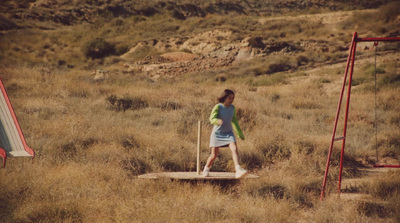 a woman walking across a dry grass covered field