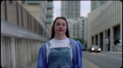 a woman standing on the side of a street next to tall buildings