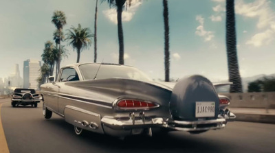 a silver car driving down a street next to palm trees