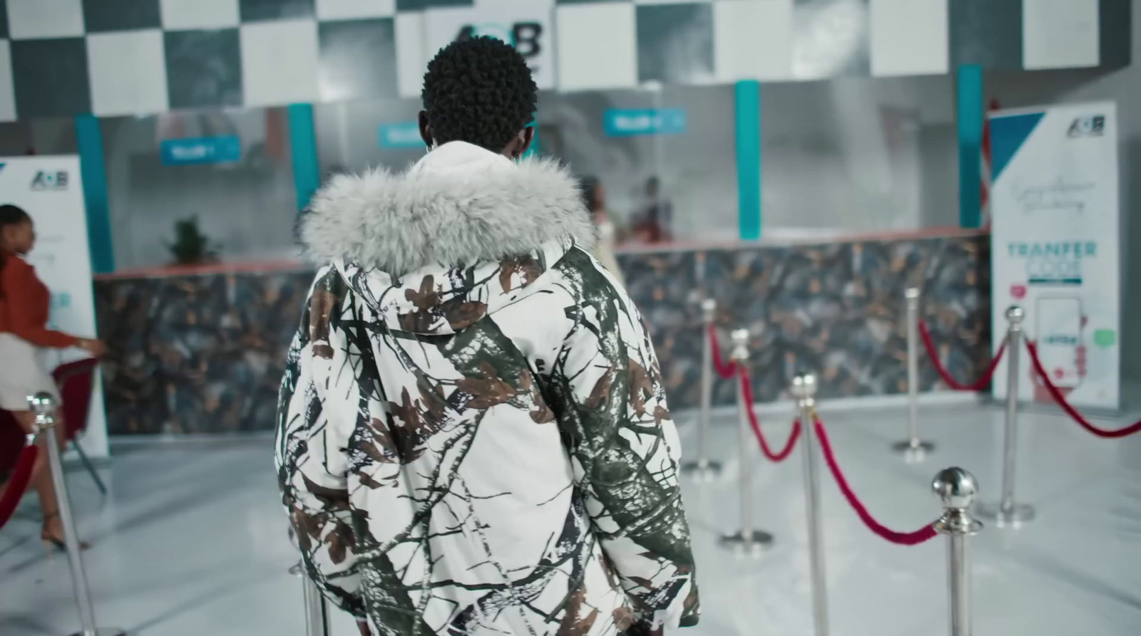 a man in a camouflage jacket is standing in front of a checkered wall