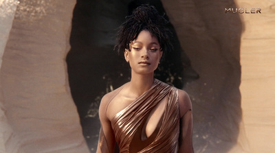 a woman in a gold dress standing in front of a rock formation