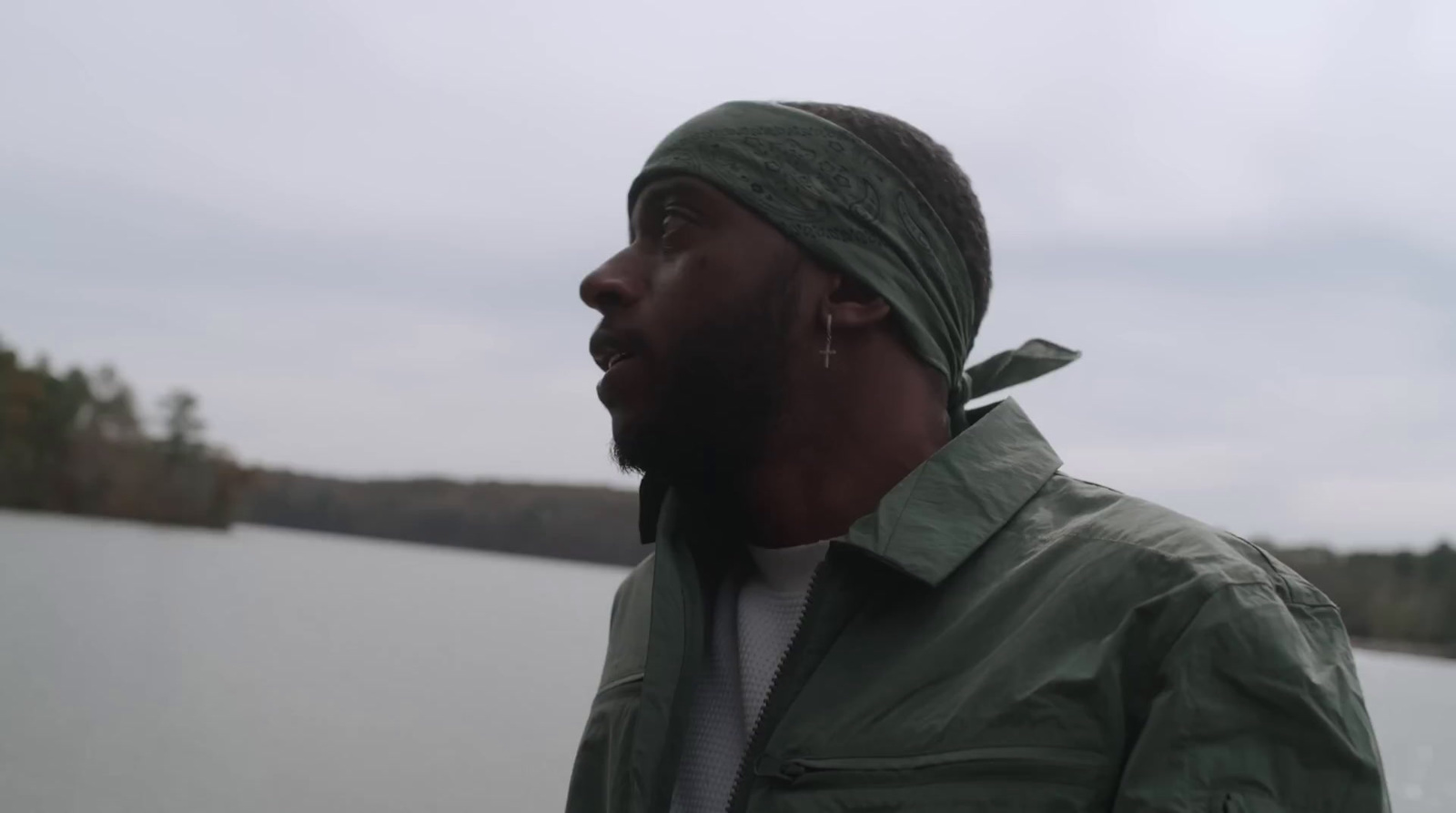 a man in a green jacket standing by a body of water