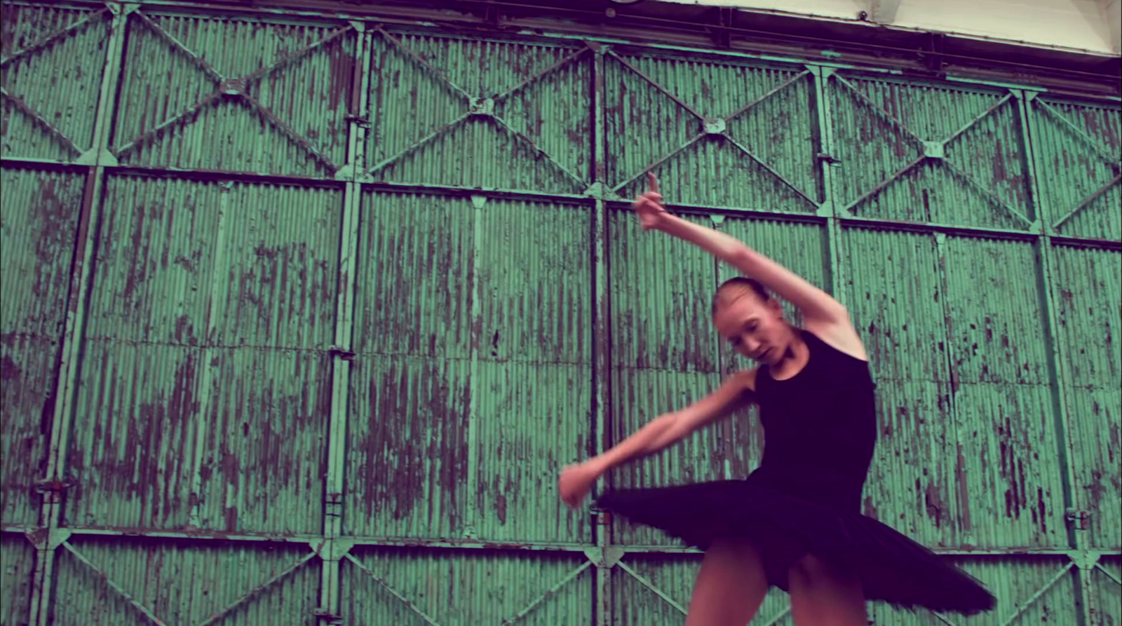 a woman in a black dress is dancing in front of a green wall