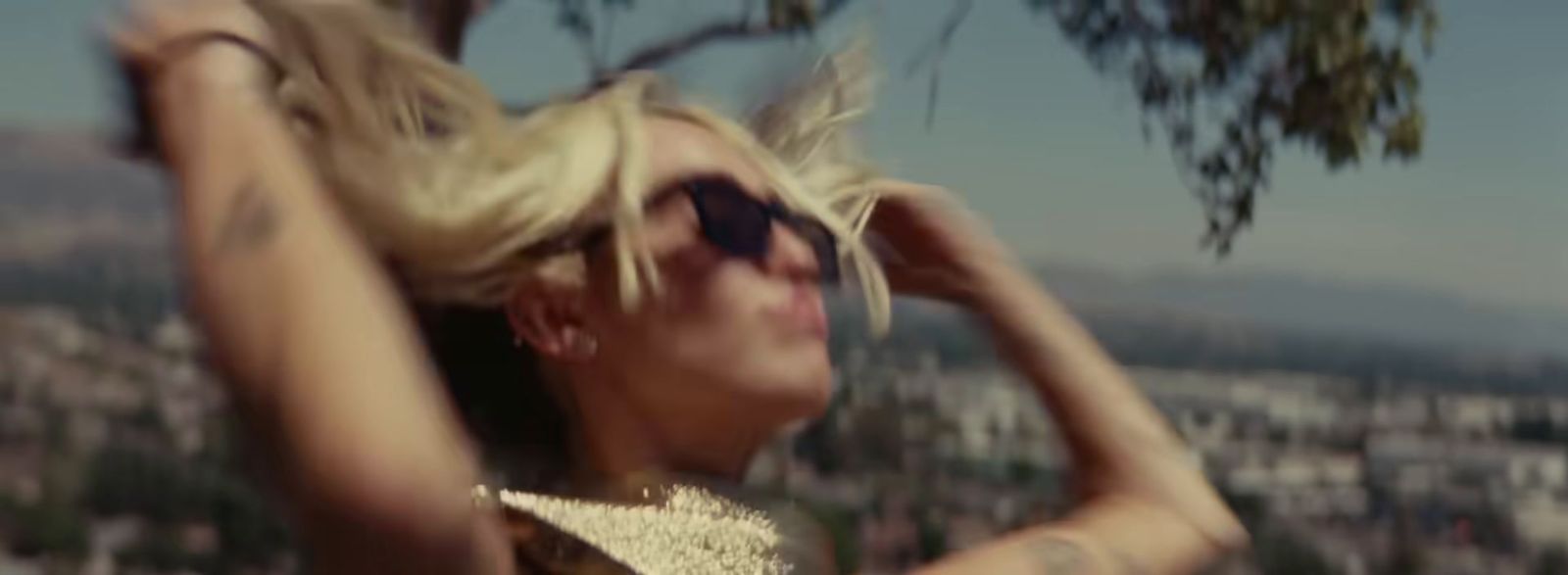 a woman with blonde hair and sunglasses on top of a hill