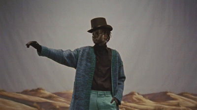 a man in a top hat and blue cardigan standing in front of a painting