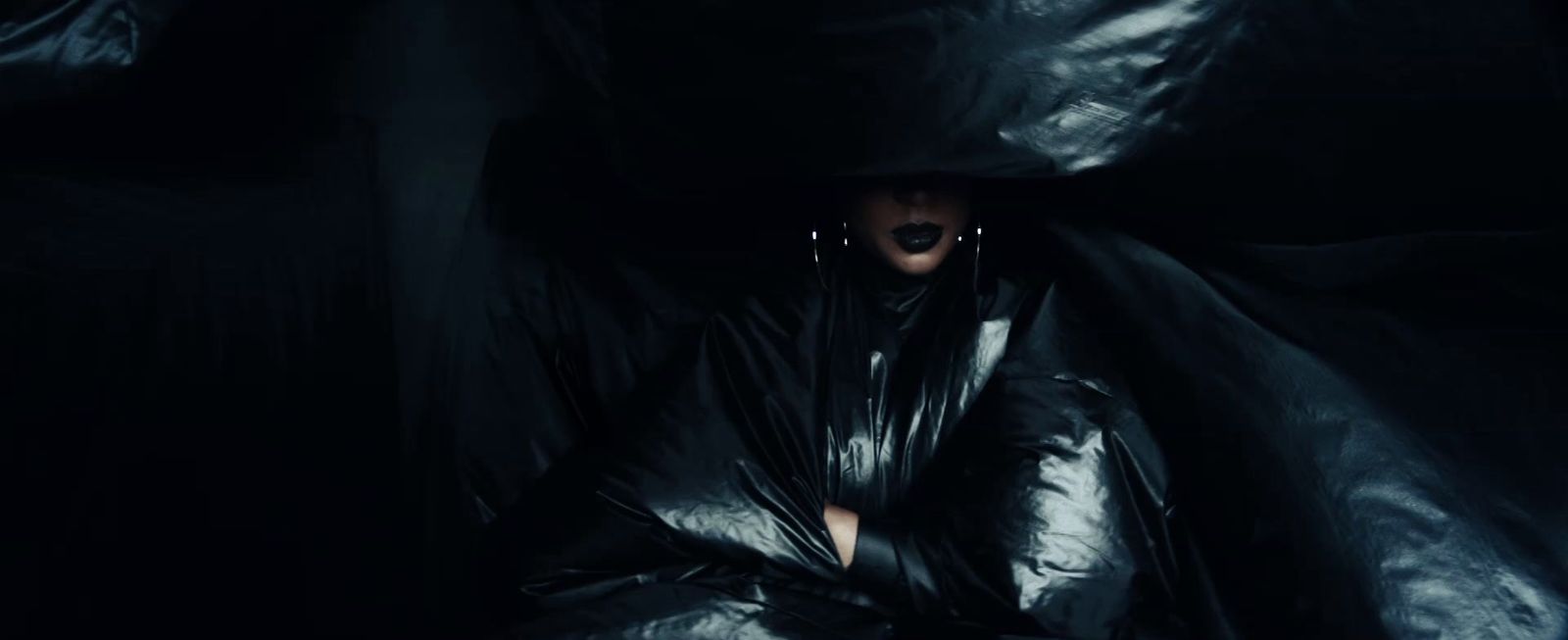 a woman in a black leather outfit hiding in a dark room