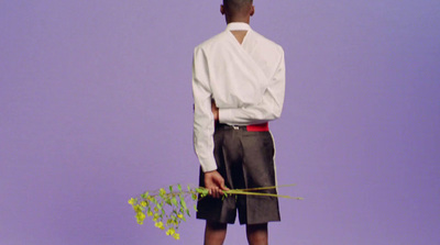 a man standing in front of a purple wall holding a flower