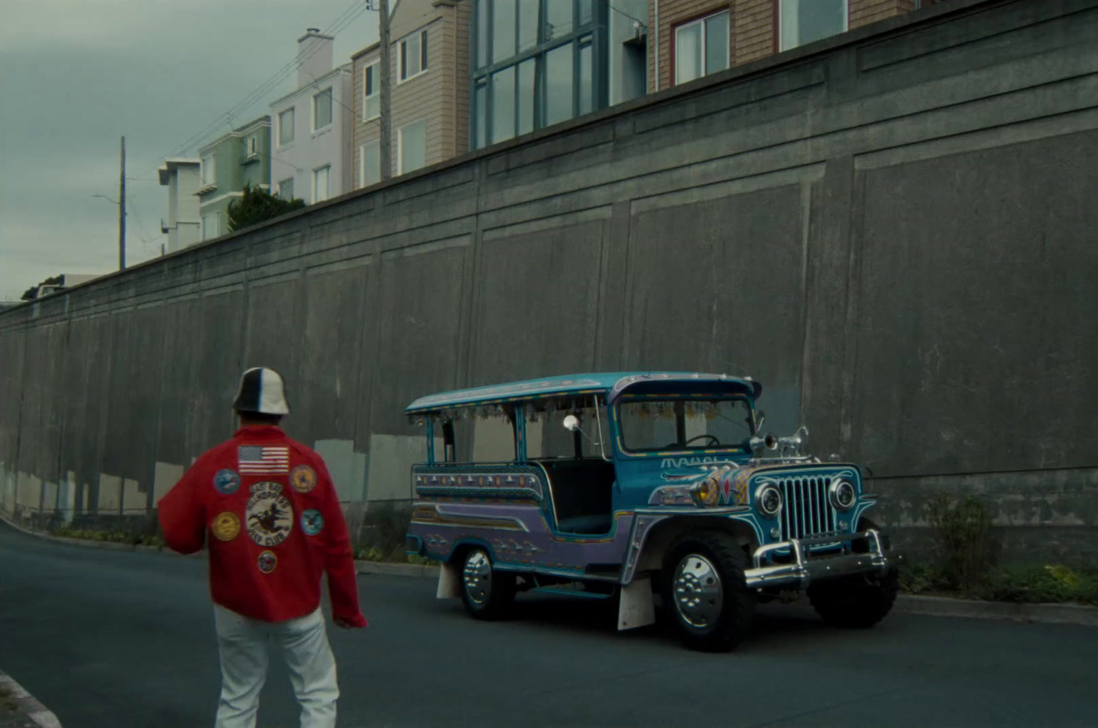 a man in a red jacket walking past a blue bus