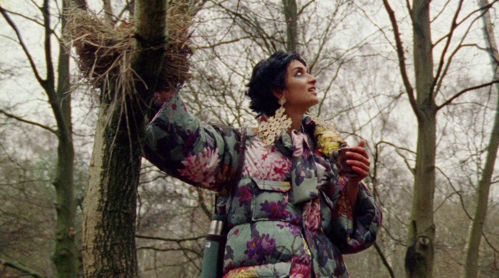 a woman standing in the woods with a bird nest in her hand