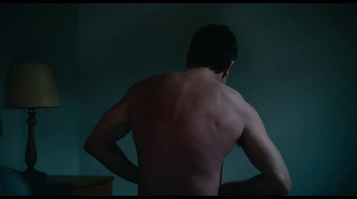 a shirtless man standing in a dark room