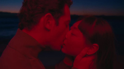 a man and a woman kissing in front of the ocean