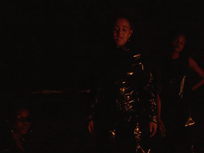 a woman standing in the dark with another woman behind her