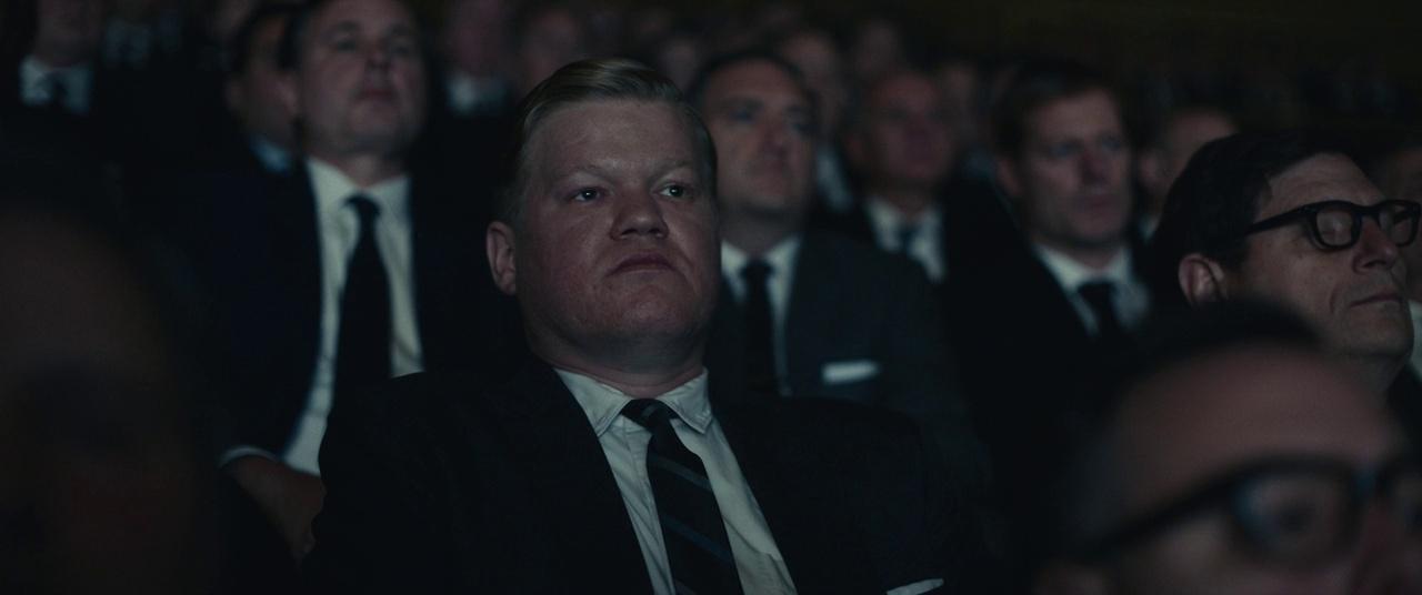 a man in a suit and tie sitting in a crowd