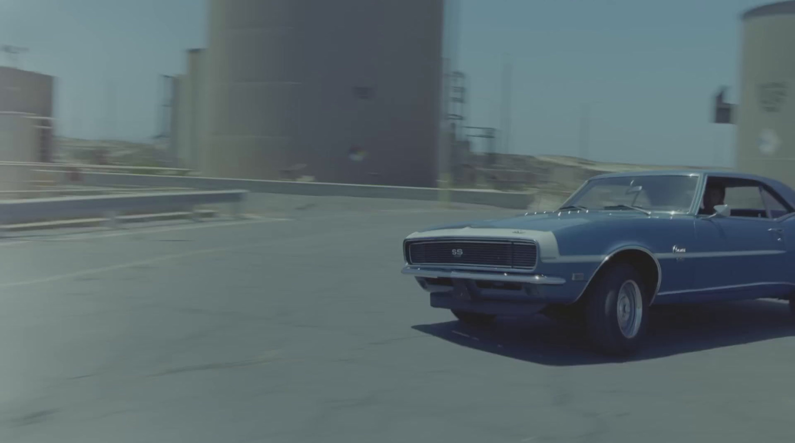 a blue car driving down a street next to tall buildings