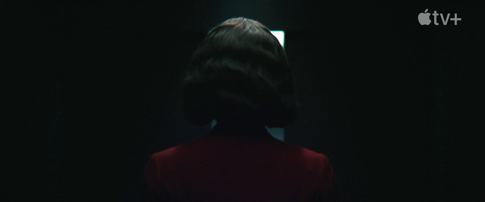 a woman standing in a dark room looking at a mirror