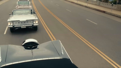 a couple of cars driving down a street next to a bridge