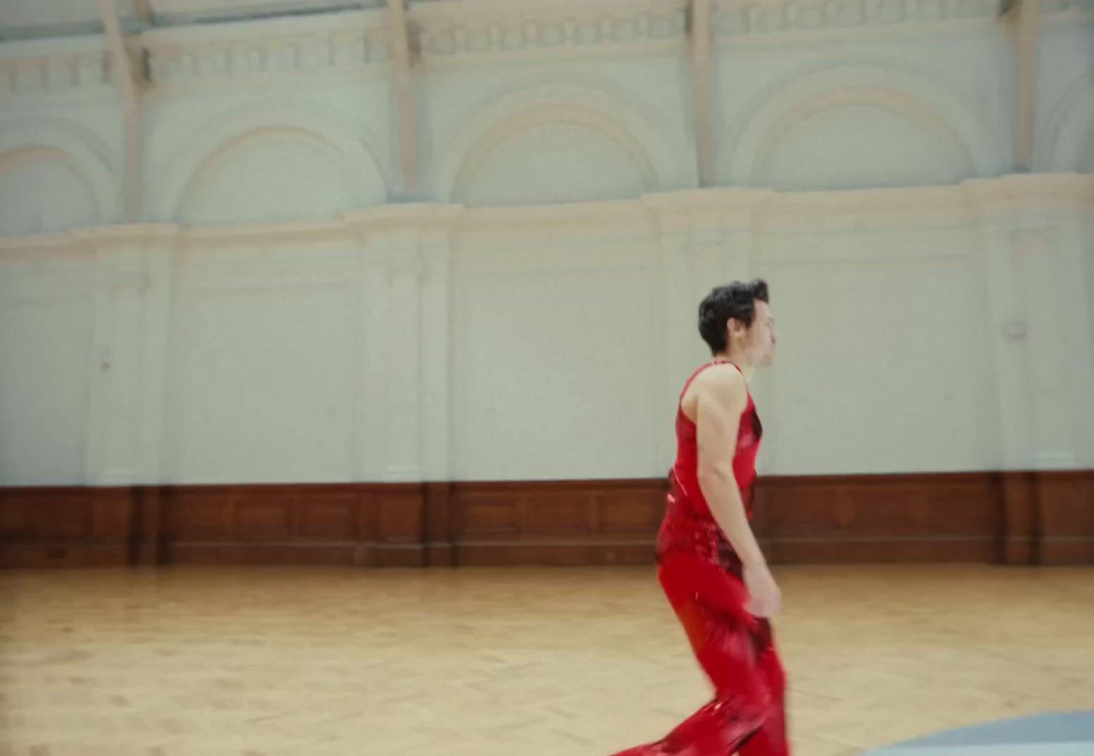 a woman in a red dress walking across a wooden floor