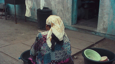 a woman sitting on the sidewalk next to a trash can