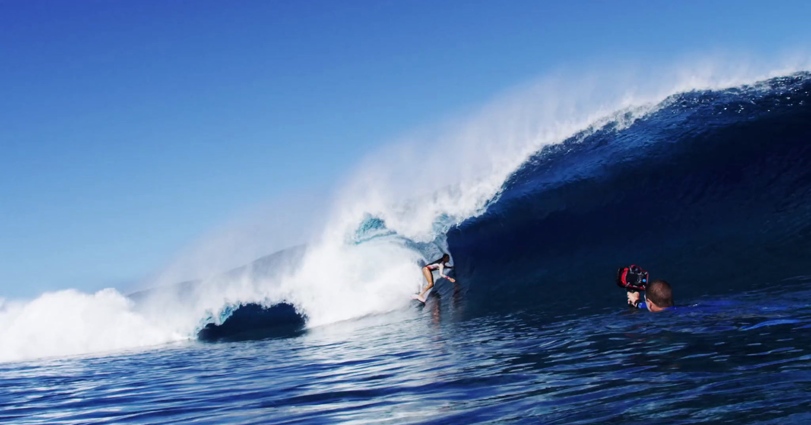 a couple of people riding a wave on top of a surfboard