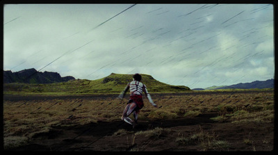 a man walking across a lush green field under a cloudy sky