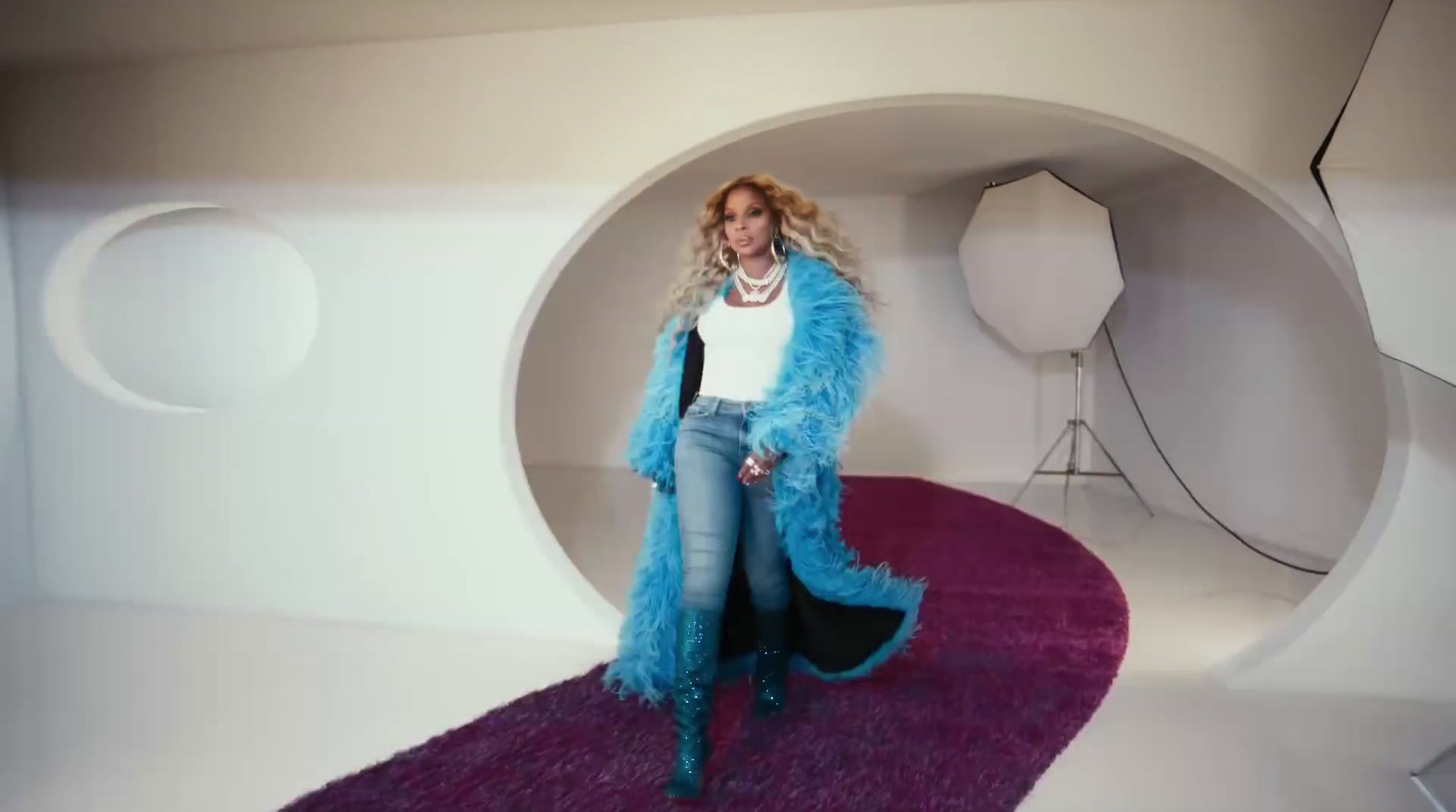 a woman in a blue coat standing in a white room