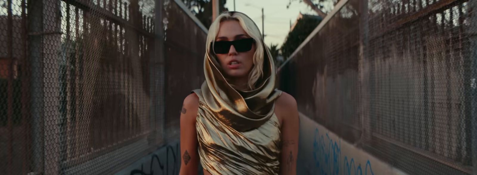 a woman wearing a scarf and sunglasses walking down a street