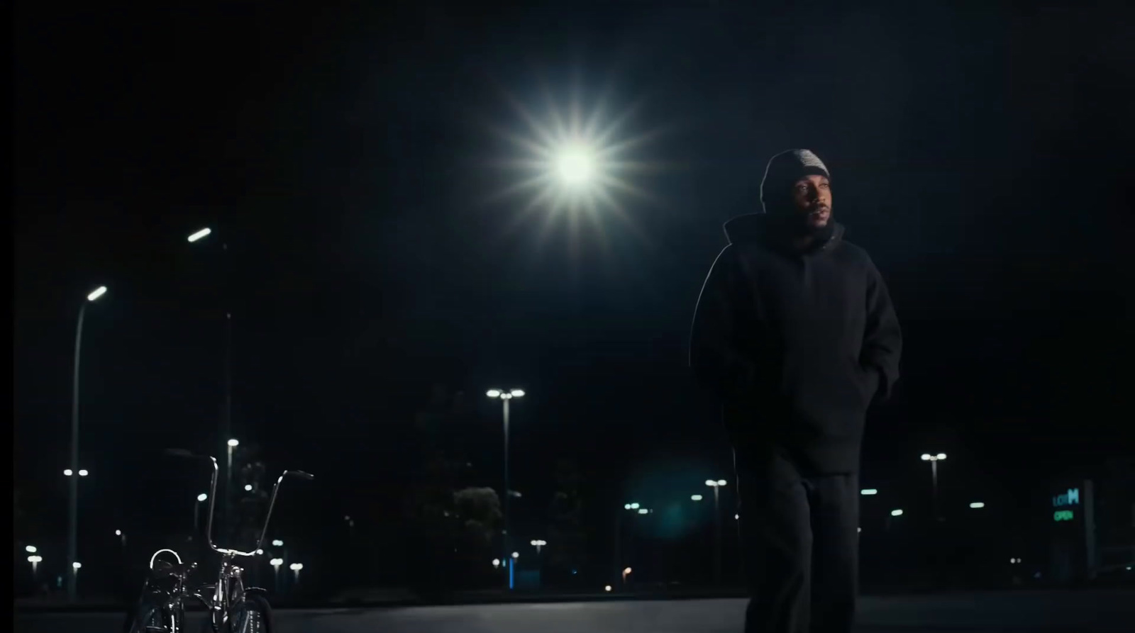 a man in a hoodie standing on a street at night