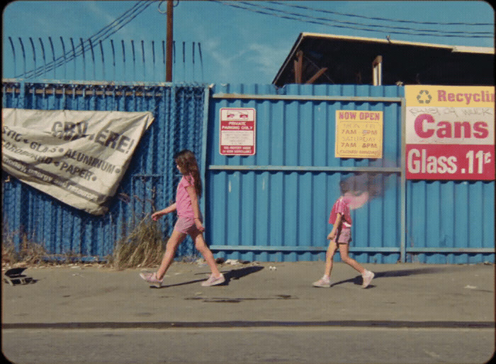 two little girls walking down the street in front of a blue fence