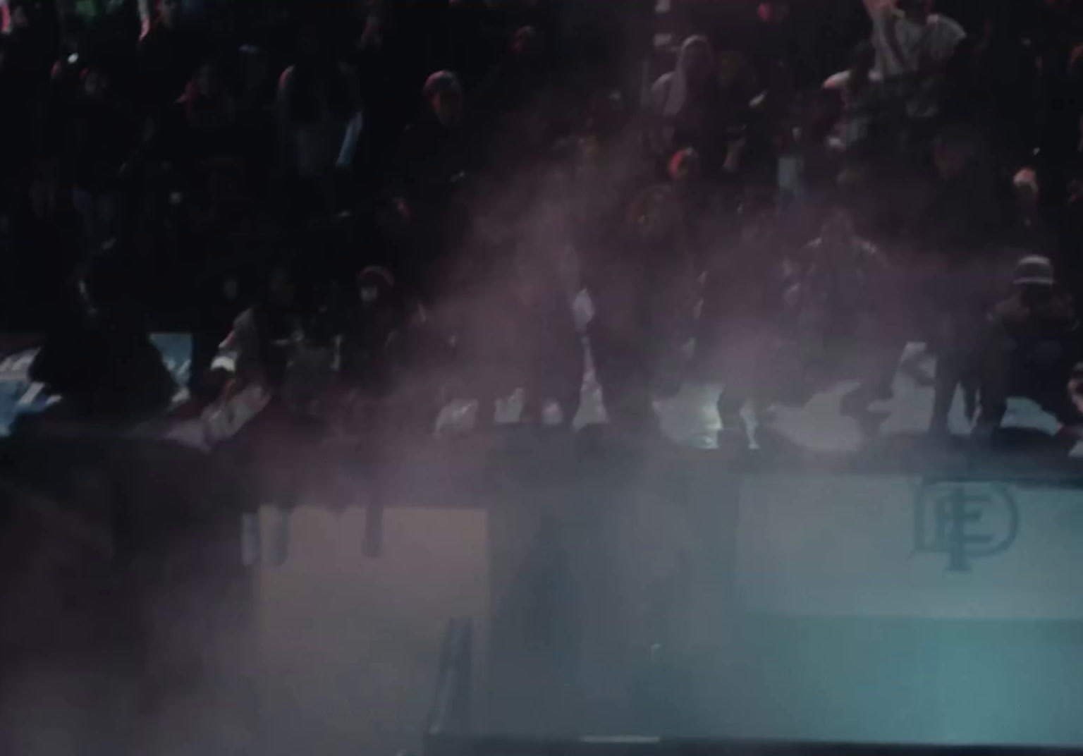 a crowd of people standing around a stage with smoke coming out of it