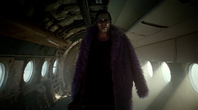 a man in a purple fur coat standing in an airplane