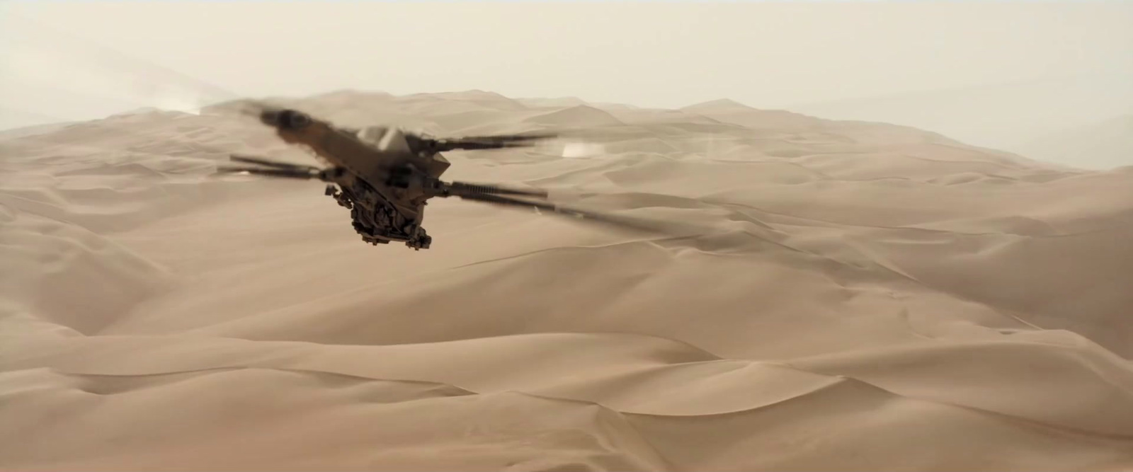 a helicopter flying over a desert covered in sand