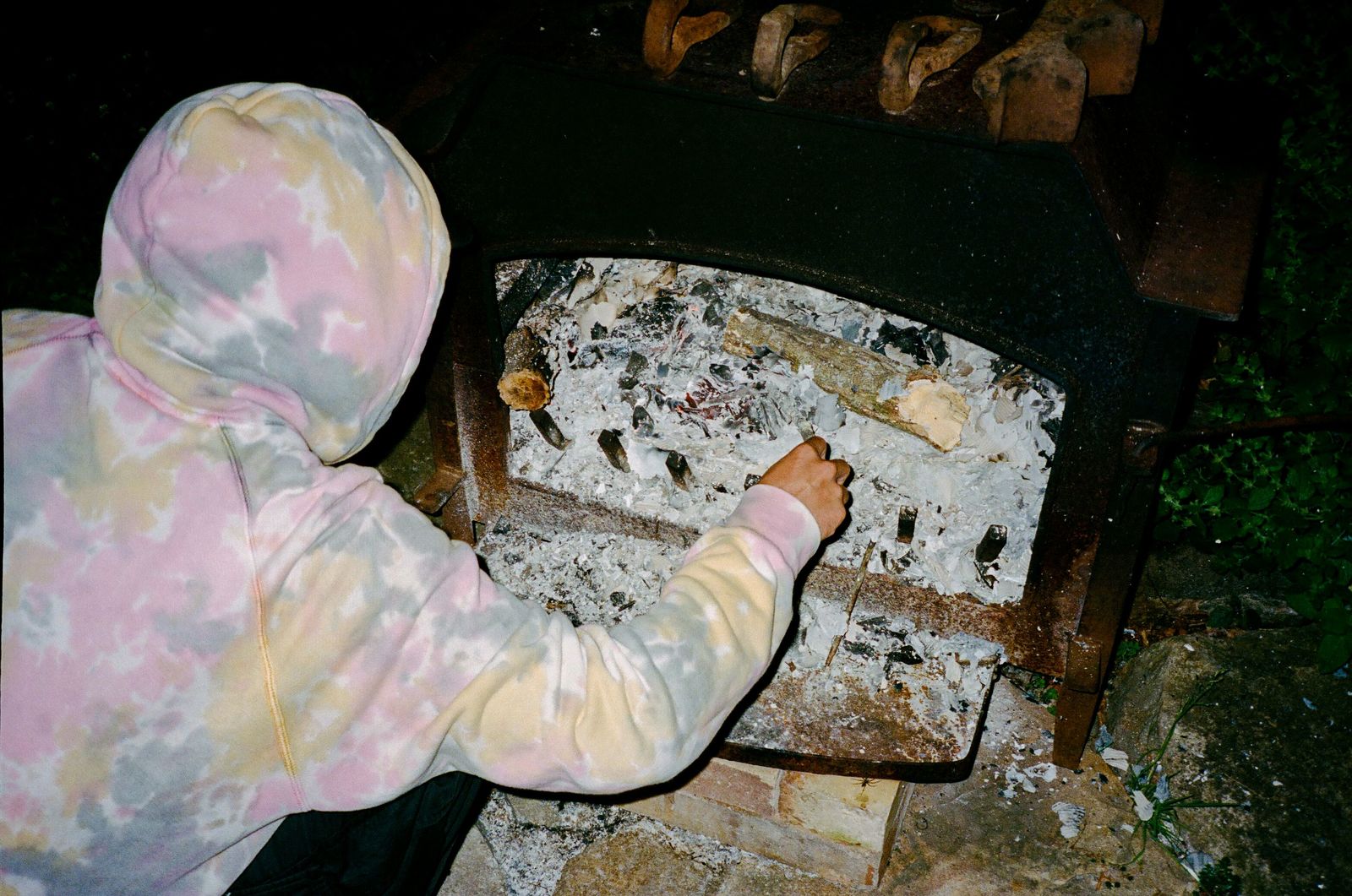 a person in a pink and yellow hoodie is putting something in a brick oven