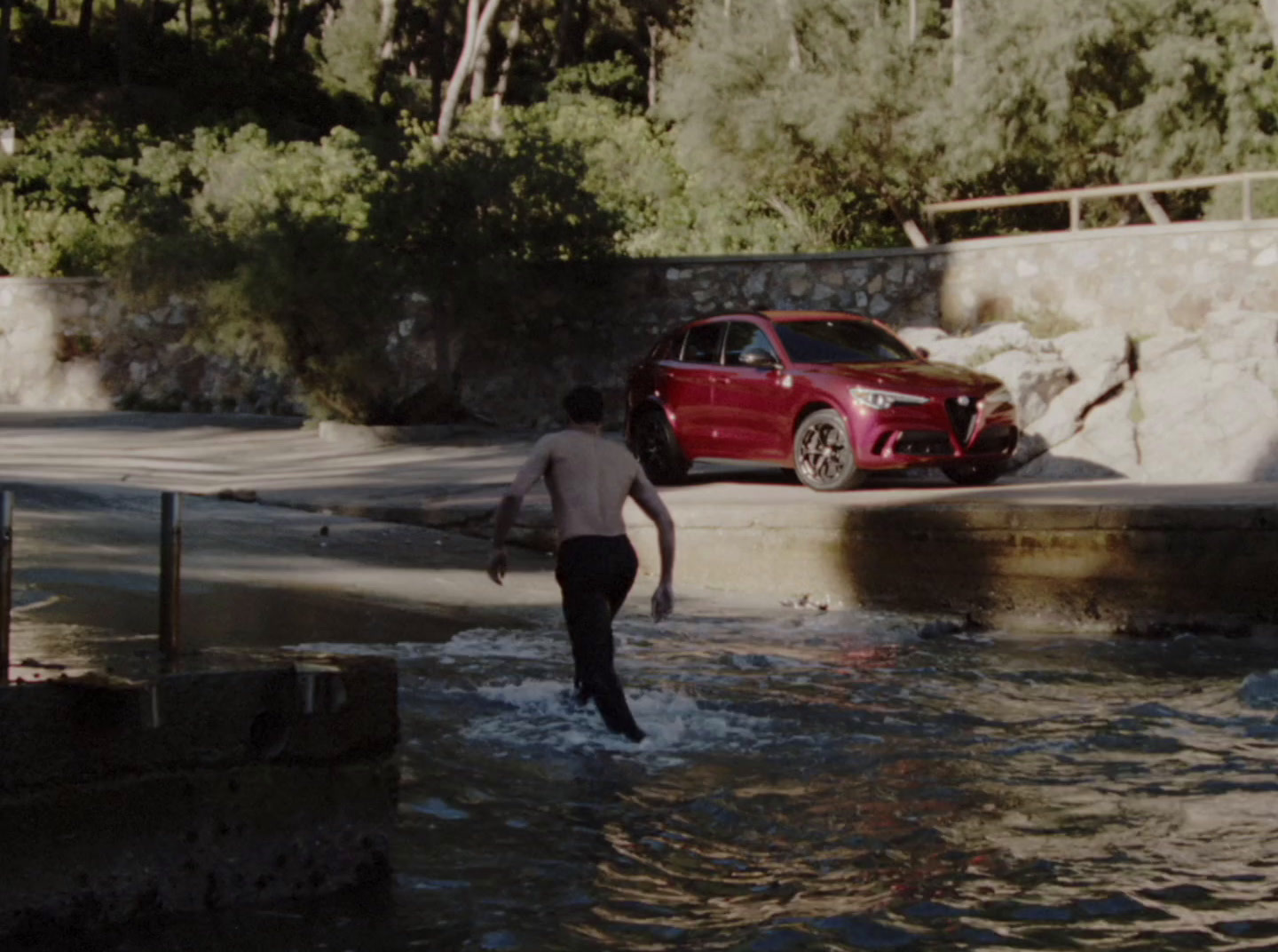 a man walking into a body of water next to a red car