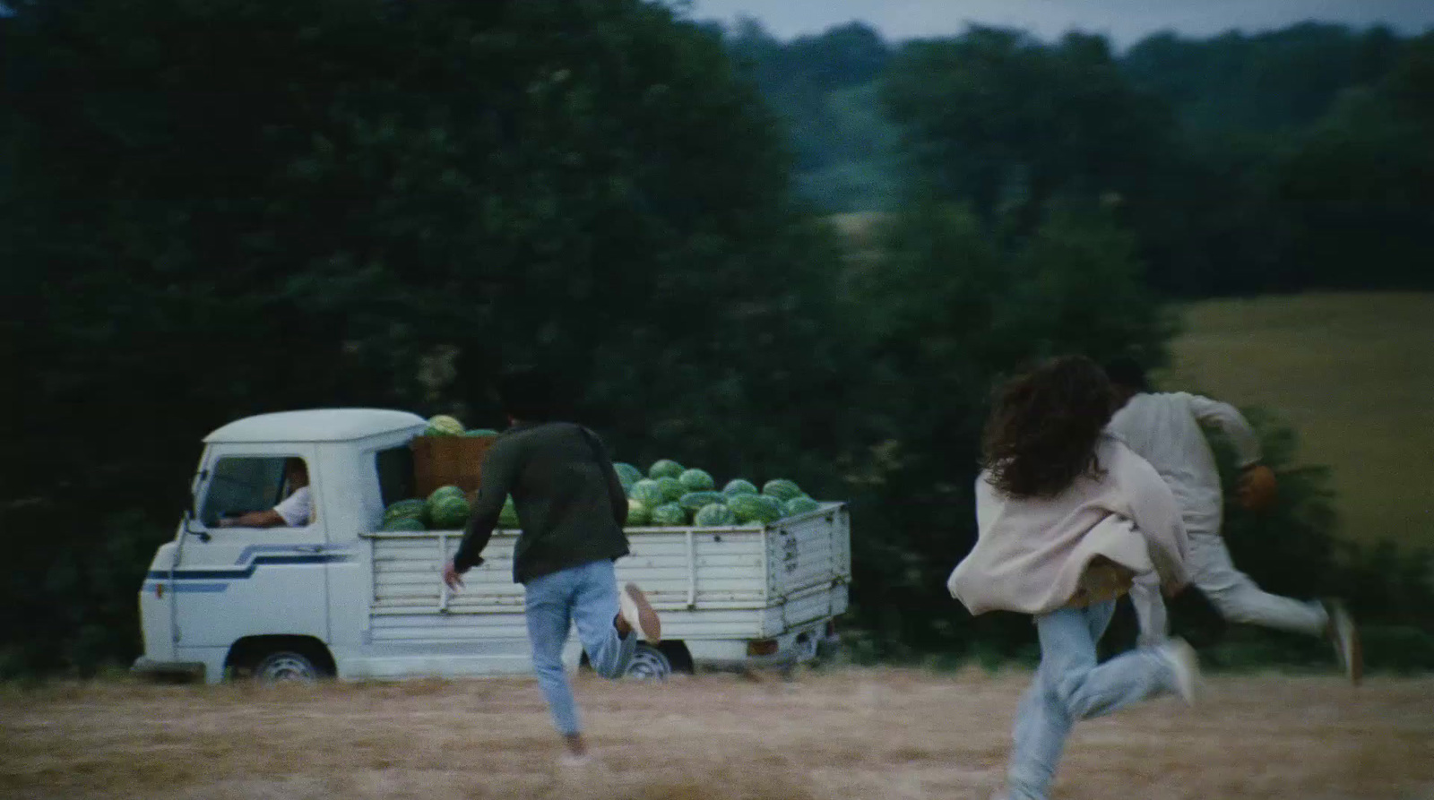 a man and a woman running towards a truck full of fruit