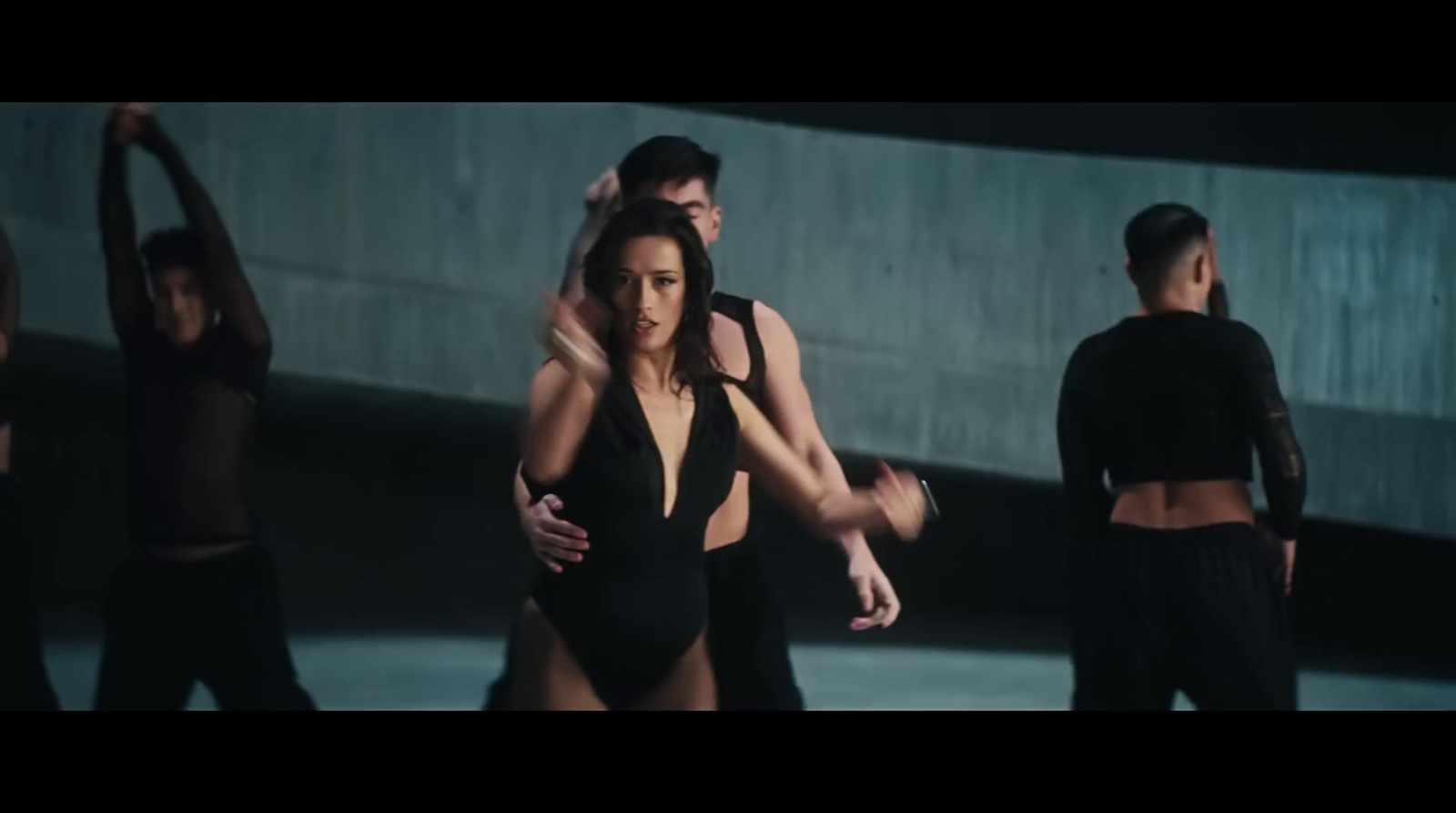 a woman in a black bodysuit standing in front of a group of dancers