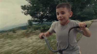 a young boy riding a scooter down a road