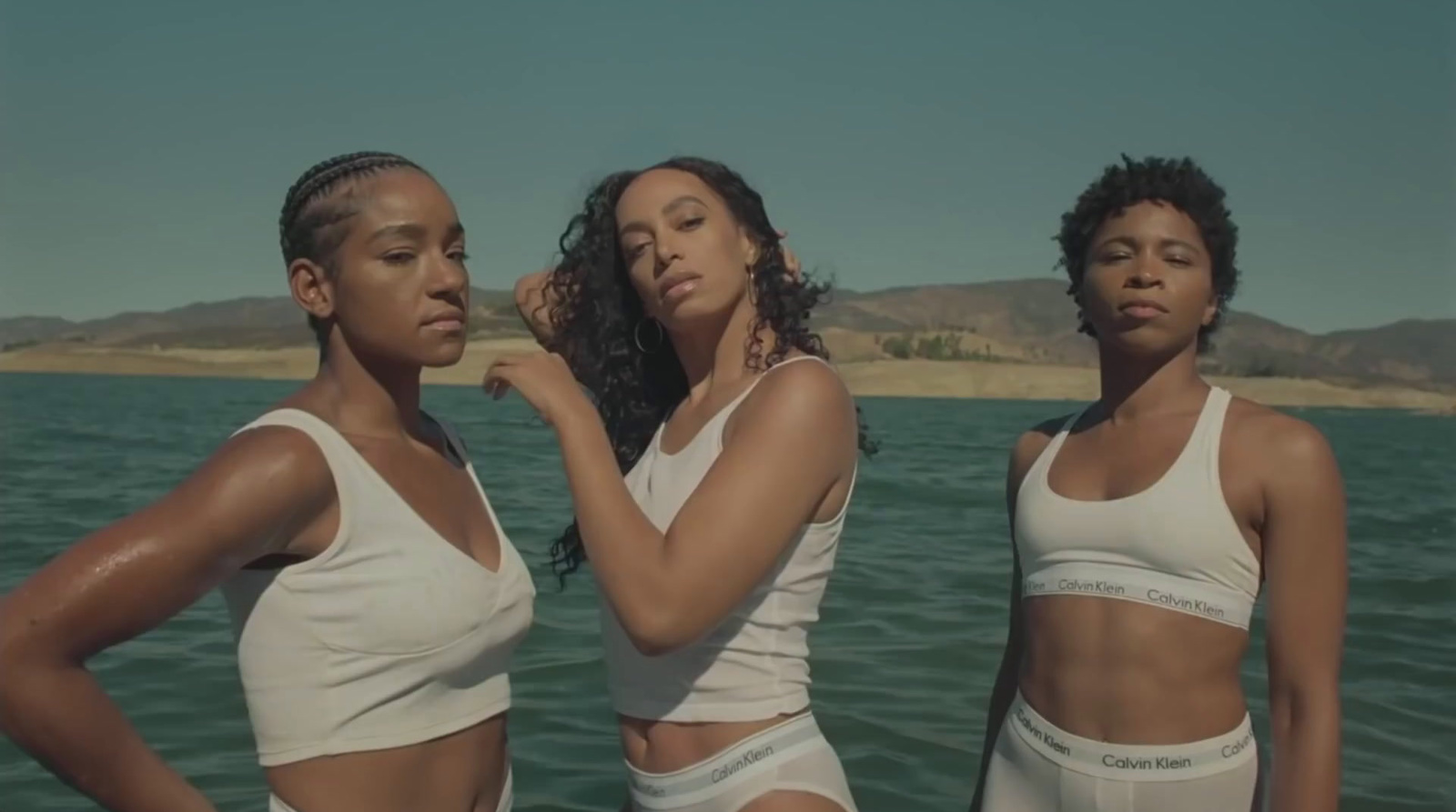 three women standing in front of a body of water