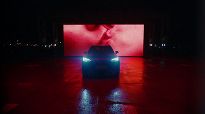 a car is parked in front of a large screen