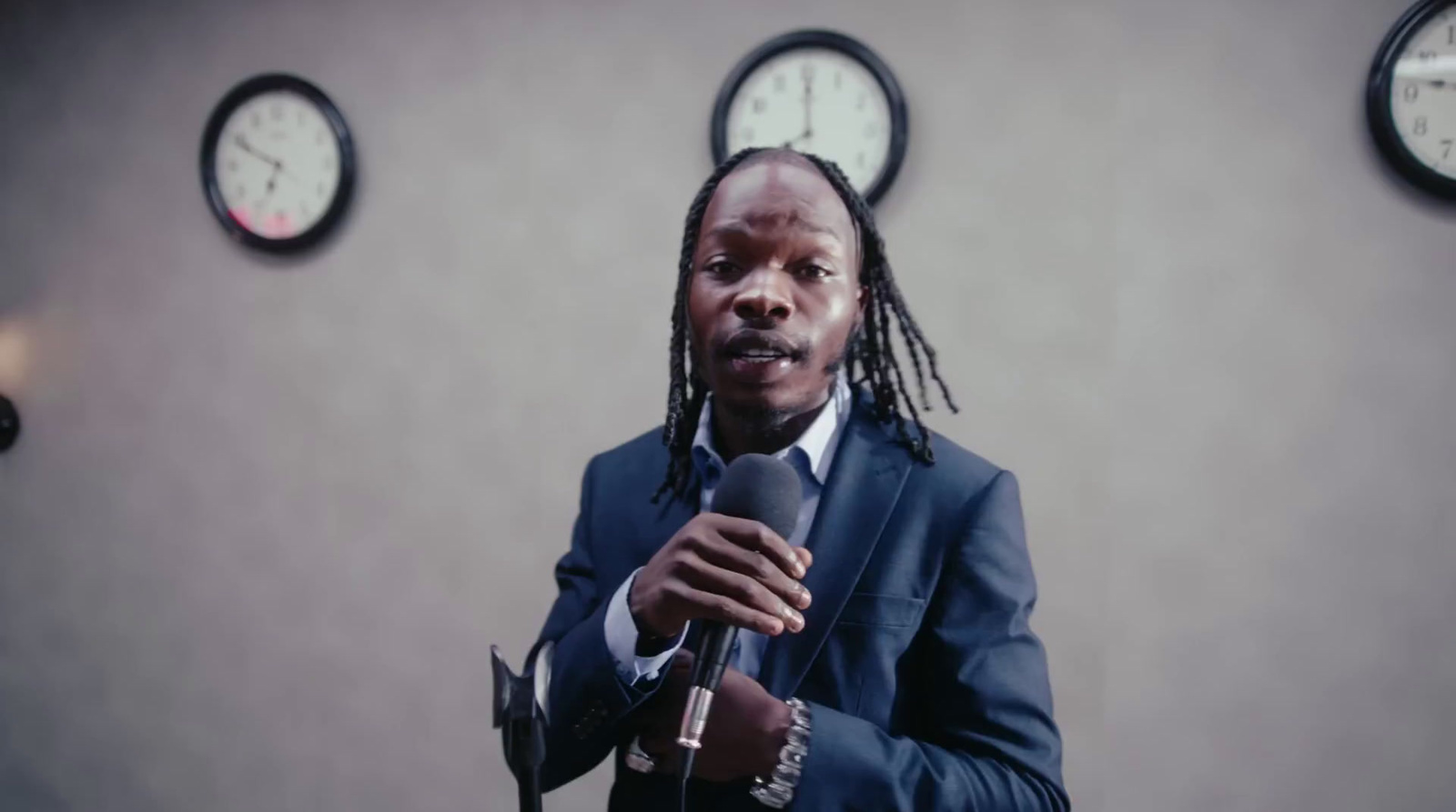 a man holding a microphone in front of three clocks