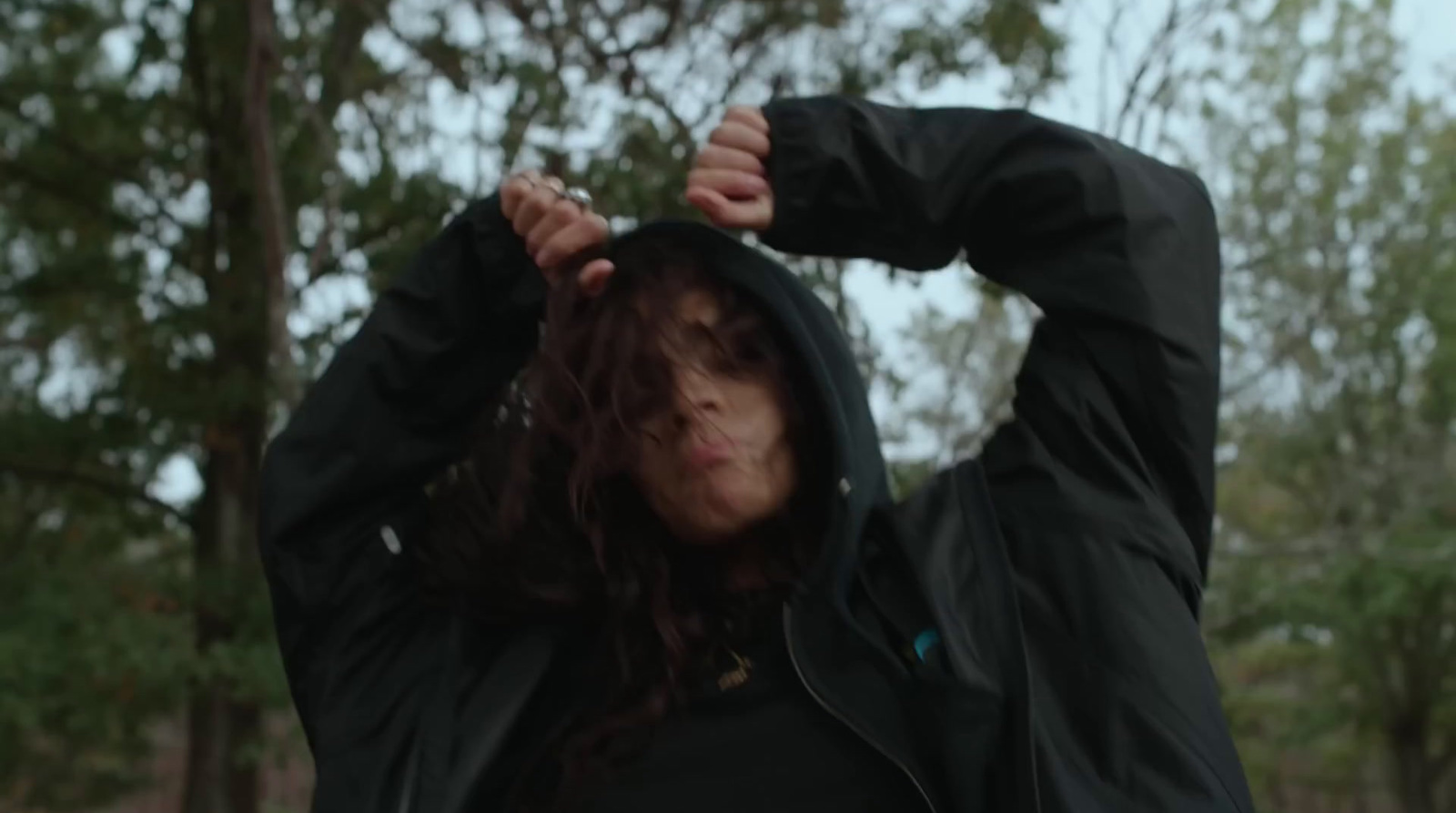 a woman in a black jacket is holding her hood up