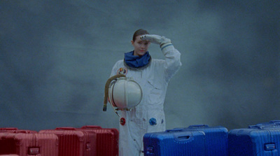 a woman in a white space suit standing in front of a bunch of suitcases