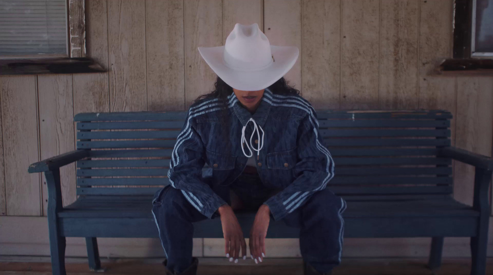 a woman sitting on a bench wearing a cowboy hat